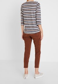 Striped long-sleeve top in navy and beige with three-quarter sleeves; paired with brown tapered pants. Casual footwear visible.