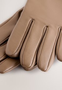 Guanti in pelle marrone esposti con quattro dita allungate, trama liscia e cuciture dettagliate lungo i bordi.