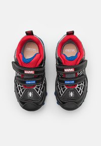 Sneaker neri con accenti rossi e blu, caratterizzati da un design in rete, strap in Velcro e un motivo a ragnatela. Progettati per la traspirabilità.