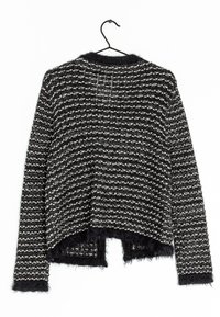 Suéter de punto texturizado en blanco y negro con mangas largas y borde de flecos, colgado en un gancho negro contra un fondo blanco.