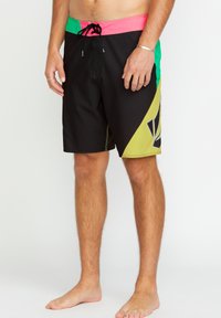 Shorts de bain noirs avec des accents verts et roses, dotés d'une taille à cordon de serrage, d'un design géométrique et d'une texture lisse.
