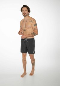 Pantaloni da nuoto neri con chiusura a cordoncino, un logo in basso a sinistra e un tessuto leggero; il modello ha tatuaggi visibili.
