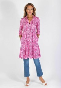 Różowa tunika w wzór paisley z rękawami o długości trzy czwarte, z bocznymi kieszeniami, zestawiona z niebieskimi dżinsami i białymi sandałami.