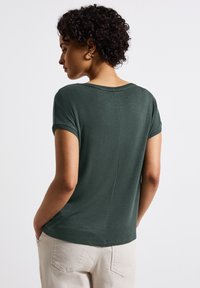 Top corto verde scuro a maniche corte con scollatura rotonda, morbido al tatto e taglio dritto, mostrato dal retro con polsini finti e dettagli delle cuciture.
