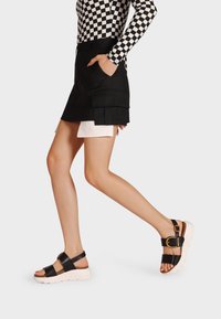 Sandali in pelle nera con una larga fascia, fibbia regolabile e suola bianca spessa. Il design presenta una texture liscia e uno stile minimalista.