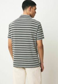 Camicia a maniche corte in bianco e nero a quadri. Realizzata in tessuto intrecciato, presenta un colletto e linee orizzontali e verticali equidistanti.