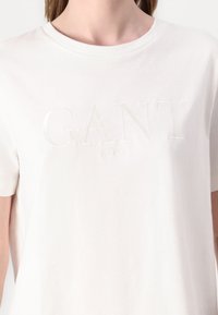 Hvid bomulds t-shirt med korte ærmer, der har et prægede "GANT" logo og teksten "NEW HAVEN" nedenfor i en subtil glans.