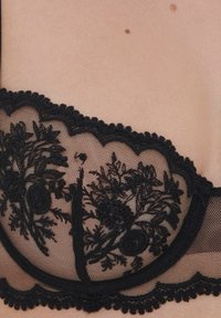 Sort blonde bh med blomsterbroderi, bølgede kanter og et gennemsigtigt mesh-design. Tekstureret blondeoverlag med kontrasterende glatte paneler.