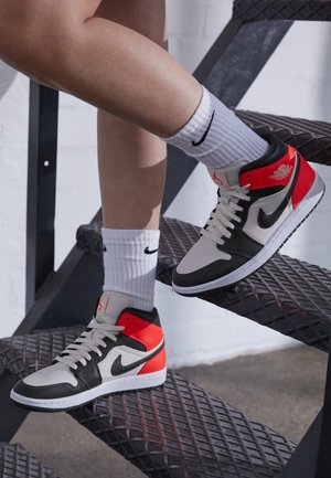 Jambes portant des chaussettes blanches Nike et des baskets Air Jordan noires, blanches et rouges sur un escalier métallique avec des marches en tôle larmée.