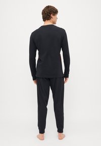Schwarzes Langarmshirt und passende Hose aus weichem Stoff. Das Shirt hat einen Rundhalsausschnitt. Die Hose hat elastische Bündchen und eine lässige Passform.