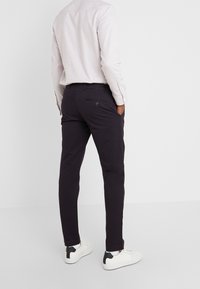 Ciemnofioletowe chinosy wykonane z bawełnianej mieszanki. Posiadają tylne kieszenie z guzikami, dopasowany krój i gładką fakturę. Noszone z jasną koszulą.