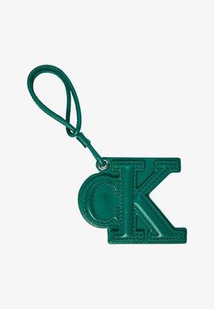 Groene leren sleutelhanger in de vorm van overlappende kleine "d" en hoofdletter "K" met een lusvormige band eraan bevestigd.