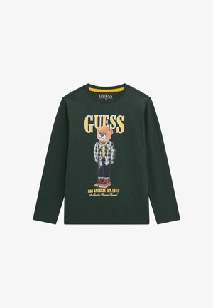 Långärmad grön bomullströja med ett motiv av en björn i rutigt skjorta och stövlar, med "GUESS" logotyp och varumärkesdetaljer i gult och vitt.