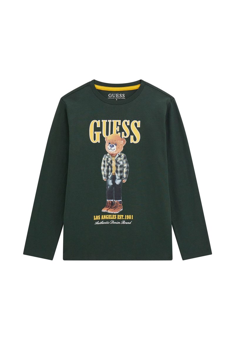 Un tricou verde din bumbac cu mânecă lungă, având un grafic cu un urs îmbrăcat în cămașă tartan și bocanci, cu logo-ul "GUESS" și detalii ale mărcii în galben și alb.