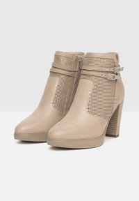 Bottes chelsea beiges en matériau synthétique texturé, dotées de panneaux en maille, de fermetures éclair sur les côtés et de talons empilés. Deux fines sangles avec boucles.