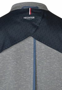 Graues Hemd mit einem gemusterten marineblauen yoke, blauen Akzenten und dem Etikett "HECHTER PARIS". Verfügt über strukturierten Stoff und moderne Designelemente.