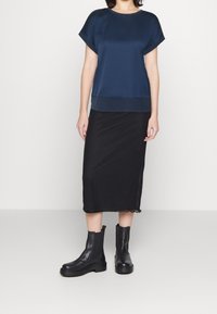 Top corto in satin blu navy con scollatura rotonda, abbinato a una gonna midi nera con orlo scallop e stivali alla caviglia neri in pelle.