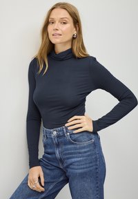 Marineblå langærmet turtle neck lavet af blød, strækbar stof, parret med høj talje blå denim jeans med knap- og lynlåsclosure.