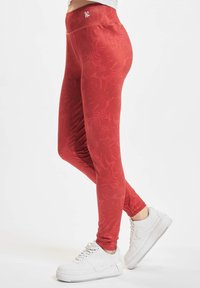 Leggings rossi con un motivo a foglia testurizzato, vita alta e design aderente, abbinati a sneakers bianche con suola spessa.