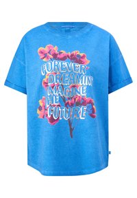 Chemise bleu à manches courtes avec des fleurs roses et jaunes et un texte blanc indiquant "Forever dreaming imagine the future" sur le devant.