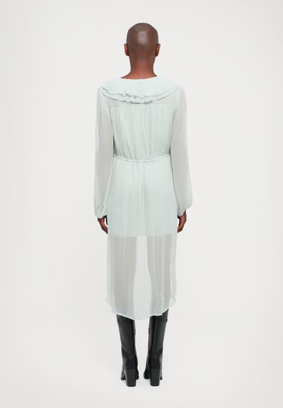 Rochie lungă, dintr-un material ușor de culoare verde mentă, cu guler volanat și talie strânsă; material semi-transparent; asortată cu cizme negre înalte.