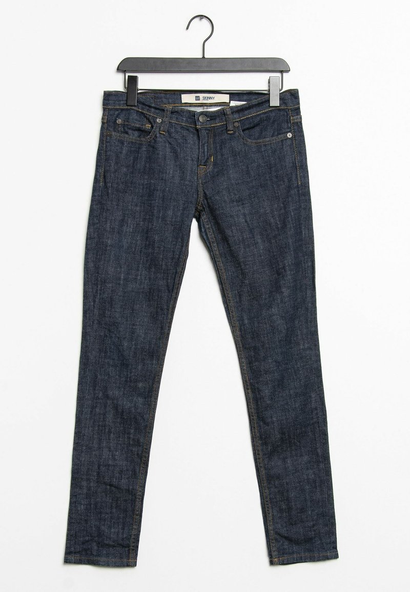 Jean skinny bleu foncé avec poches avant accroché à un cintre noir sur un fond blanc.