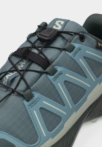 Μπλε και γκρι αθλητικό παπούτσι με μαύρα κορδόνια ταχείας έλξης, επωνυμο δέσιμο και ανθεκτικό αεριζόμενο πάνω μέρος.