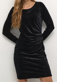 Černé sametové šaty s dlouhými rukávy, kulatým výstřihem a přiléhavým střihem. S jemným řasením po straně pro texturu.