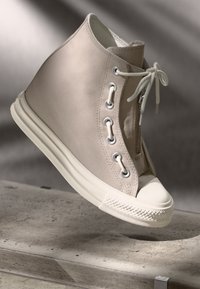 Beige høyhælte sneakers med canvasmateriale, rund tå, hvit gummis�åle og sølvfargede øyer. Har snøring og glidelås på siden.