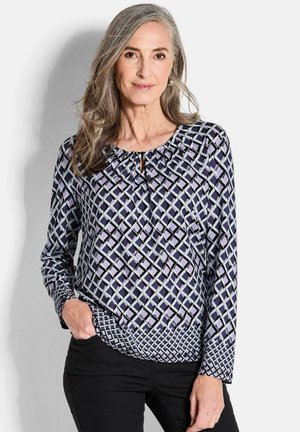 Langärmlige Bluse in Marineblau mit geometrischem Muster in Helllila und Blau. Mit einem Schlüsselanhausschnitt und gerafftem Stoff um den Hals.