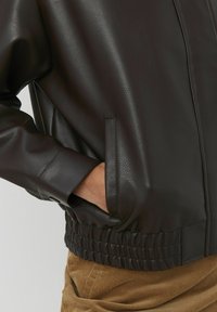 Veste en cuir noir avec une texture lisse, taille élastique et poches latérales, offrant une coupe décontractée et des détails de couture minimaux.