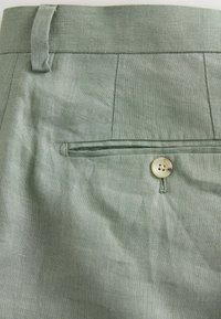 Hellgrüne Leinenhose mit flachem Frontdesign, einer Gesäßtasche mit Knopfverschluss und einer strukturierten Stoffoberfläche.