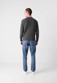 Maglione grigio a maglia con orlo a coste, abbinato a jeans in denim blu chiaro. Il modello è in piedi, leggermente rivolto a sinistra. Tessuto morbido, vestibilità casual.