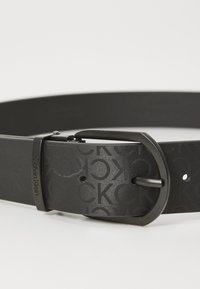 Cintura in pelle nera con motivo logo embossato, fibbia in metallo opaco e superficie liscia con fori uniformemente distanziati per la regolazione.