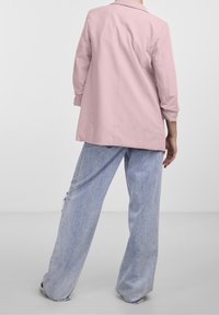 Růžový blejzer s přiléhavým střihem, tříčtvrtečními rukávy a jednopolohovým klopovým límcem, kombinovaný s volnými, světle modrými džíny.