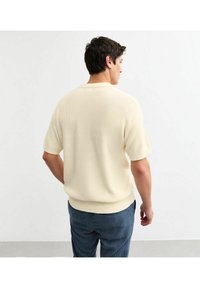 Kortemouw gebreide trui in lichtbeige met een geribbeld textuur en ronde halslijn. Gecombineerd met marineblauwe gestreepte broek.