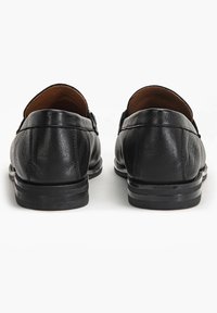 Černé kožené mokasíny s hladkým povrchem, zaobleným tvarem a nízkým podpatkem. Disponují jednoduchým zadním designem bez viditelného kovového prvku.