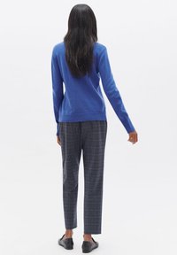 Un pull en tricot bleu avec un col rond, associé à un pantalon à carreaux gris et des chaussures noires à enfiler, vu de dos.