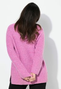 Rosa stickad tröja med ribbad textur, långa ärmar, sidsprund och en avslappnad passform, med en varierad rosa färgpalett.