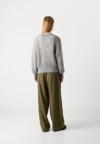 Hellgrauer, oversized Strickpullover mit Rippenstruktur und überschnittenen Schultern, kombiniert mit olivgrünen, weit geschnittenen Hosen.