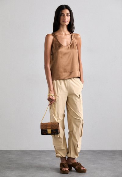 Brown satin tank top with a scoop neckline, beige cargo pants, and brown patterned handbag with gold hardware. Brown platform sandals.
