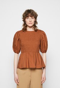 Blusa de algodão castanha com corpete franzido, mangas bufantes e bainha peplum. Apresenta um decote redondo e textura suave.