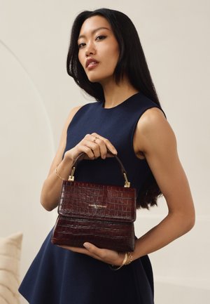 Crocodile-patterned burgundy leather handbag with a structured shape, gold hardware, and a small top handle. Brand plaque visible.