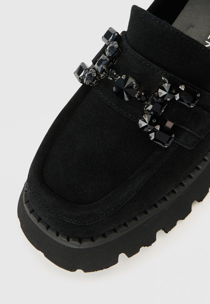 Czarne zamszowe mokasyny z ozdobnymi czarnymi kryształkami, zaokrąglonym noskiem i grubą gumową podeszwą z teksturowanym bieżnikiem.