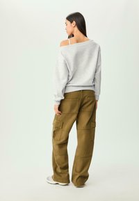 Sweat à coupe ample gris avec un design décolleté, associé à un pantalon cargo vert olive comportant plusieurs poches et une jambe large.