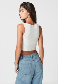 Biała prążkowana crop top z okrągłym dekoltem, w połączeniu z jasnoniebieskimi dżinsami o wysokim stanie, prezentującymi luźny krój i postrzępione wykończenie.