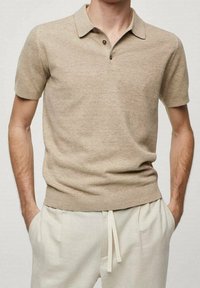 Polo shirt beige à manches courtes avec un tricot texturé, doté d'un col et d'une patte de boutonnage à trois boutons, associé à un pantalon clair.