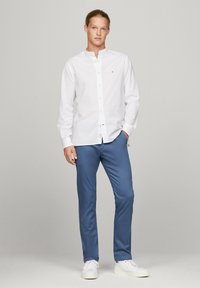 Camicia bianca con colletto, abbinata a chinos blu e scarpe da ginnastica bianche. Design semplice, texture liscia e silhouette aderente.