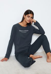 Maglietta a maniche lunghe grigio scuro e pantaloni abbinati in tessuto morbido, con il logo "Marc O’Polo" in bianco. La maglietta ha un colletto rotondo.
