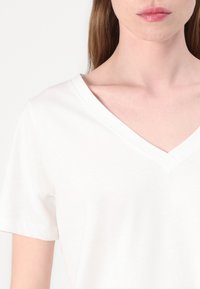 White cotton t-shirt with a v-neck design, short sleeves, and a soft texture, featuring minimal stitching and no visible patterns.